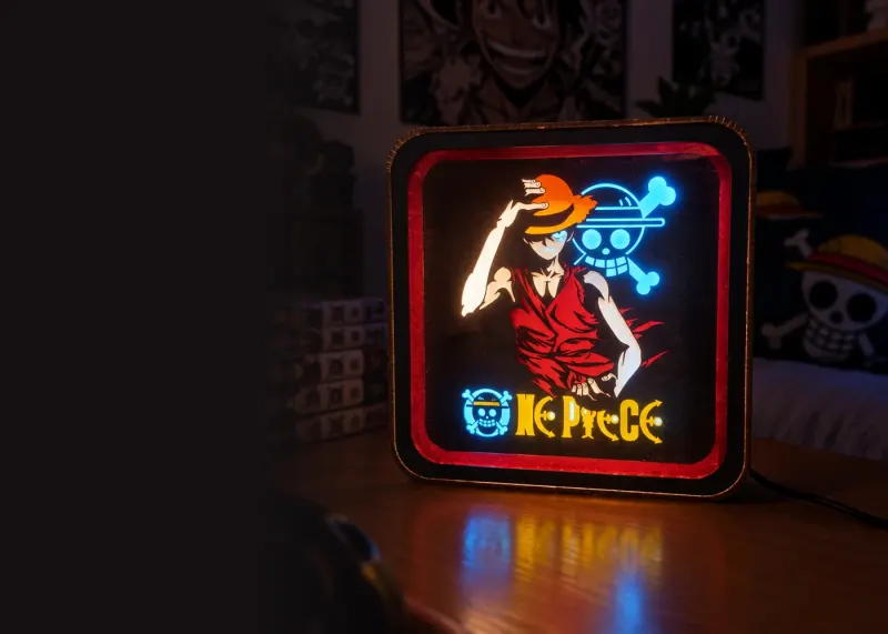 Veilleuse One Piece allumée sur un bureau, à côté de mangas